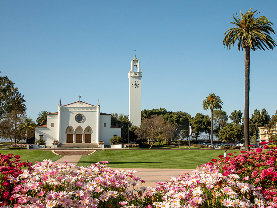 Spring flowers are seen in the foreground with Sunken Garden, Sacred Heart Chapel and the tower appear behind them.