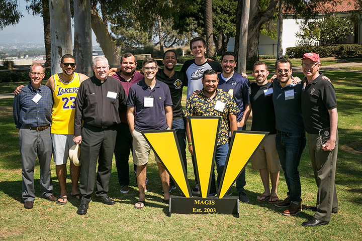 A group of alumni standing in front of a Magis sign