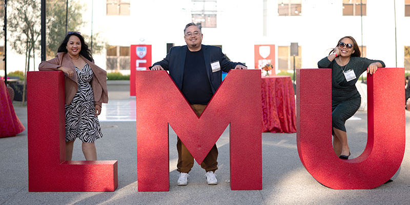 Three alumni pose with red LMU letters at Grand Reunion 2023.