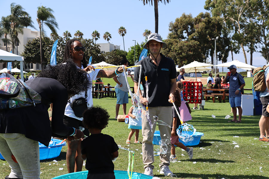 Adults and a young child gather around a bubble pit during the Alumni BBQ.