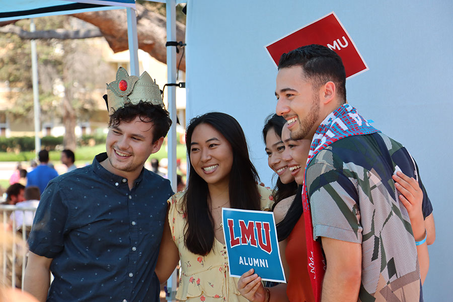 Young alumni pose in a photo booth with a sign which reads 